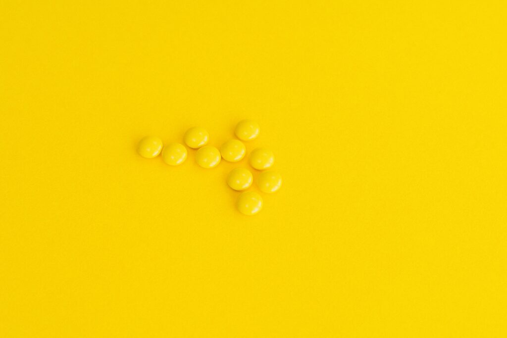 Close-up of yellow pills arranged as an arrow on a vivid yellow background.
